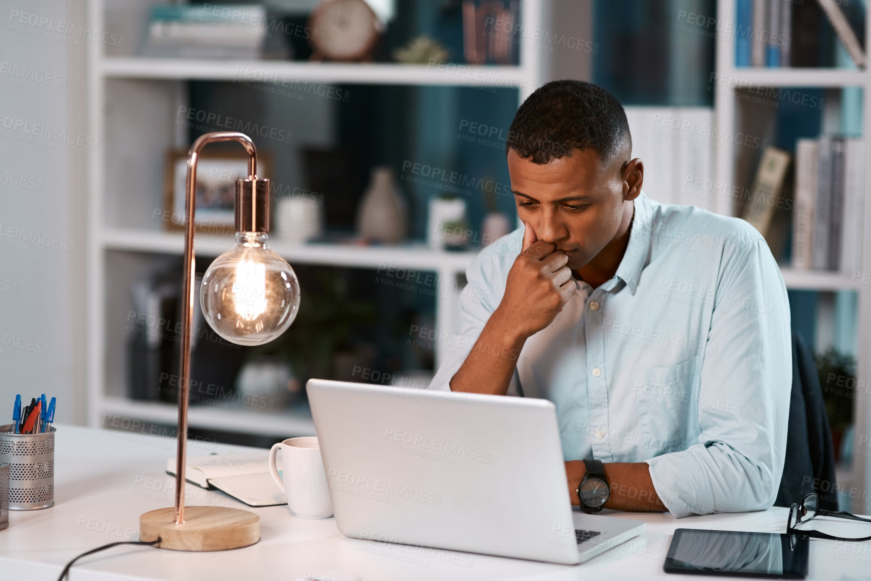 Buy stock photo Shot of a handsome young businessman working on his laptop during a late night shift at work