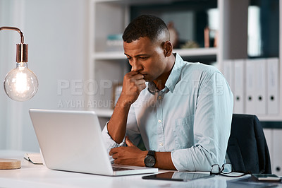 Buy stock photo Shot of a handsome young businessman looking stressed while working on his laptop during a late night at the office