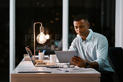 Buy stock photo Shot of a handsome young businessman using a digital tablet while working late in his office