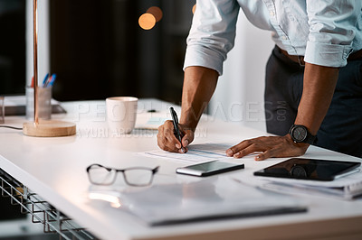 Buy stock photo Shot of an unrecognizable businessman filling out some paperwork while working late in his office