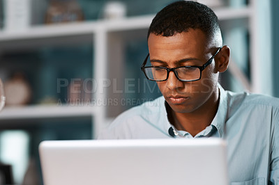 Buy stock photo Shot of a handsome young businessman working on his laptop during a late night shift at work