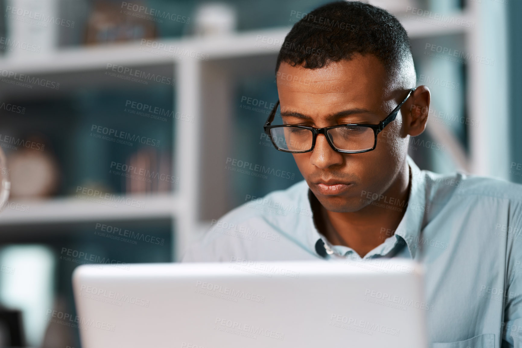 Buy stock photo Shot of a handsome young businessman working on his laptop during a late night shift at work