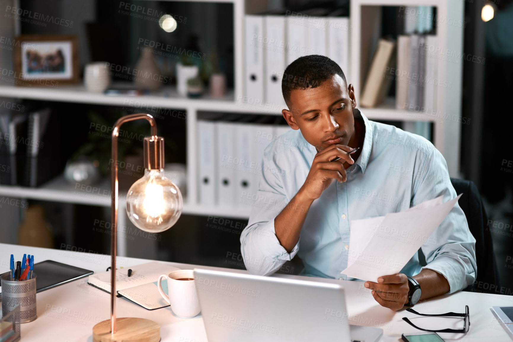 Buy stock photo Shot of a handsome young businessman going over some paperwork while working late in his office