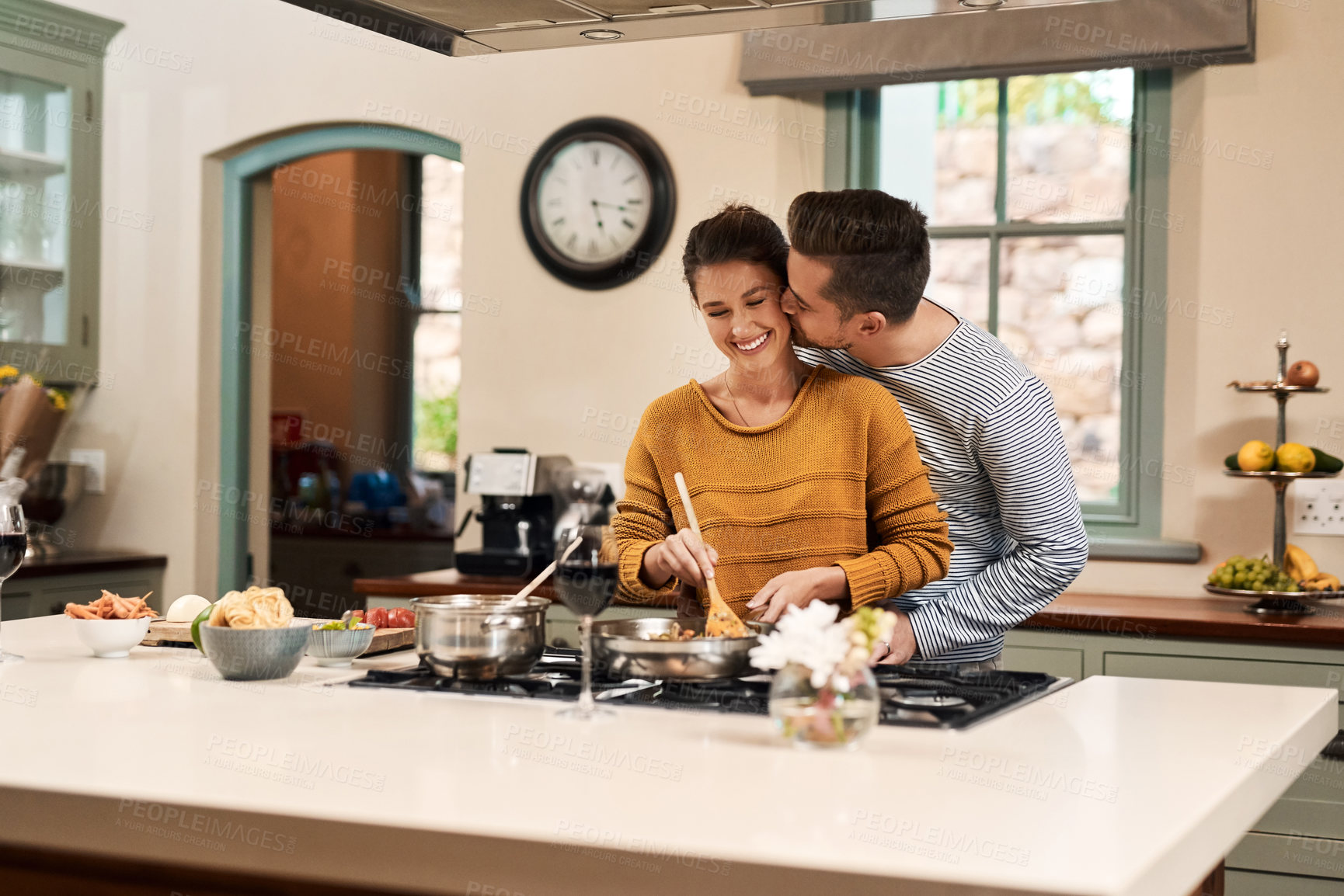 Buy stock photo Shot of an affectionate young man kissing his wife on the cheek while she prepares a meal in the kitchen at home