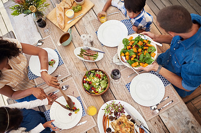 Buy stock photo High angle shot of a young family of four enjoying a meal together around a table outdoors