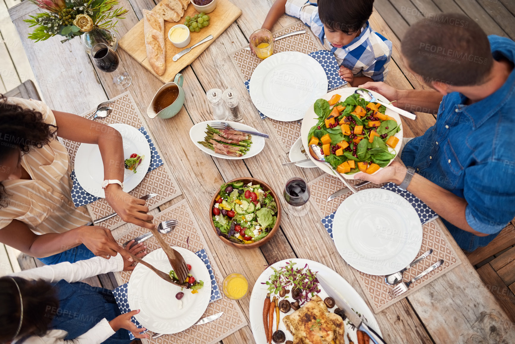 Buy stock photo High angle shot of a young family of four enjoying a meal together around a table outdoors