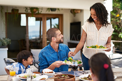 Buy stock photo Shot of a beautiful young woman dishing up salad on her husband's plate while enjoying a meal with family outdoors