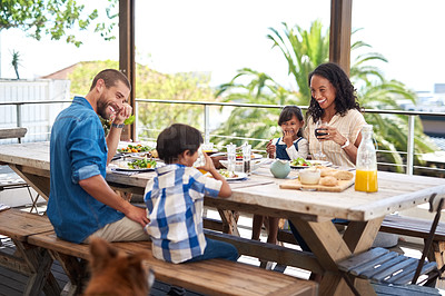 Buy stock photo Shot of a beautiful young family enjoying themselves while having a meal together around a table outdoors