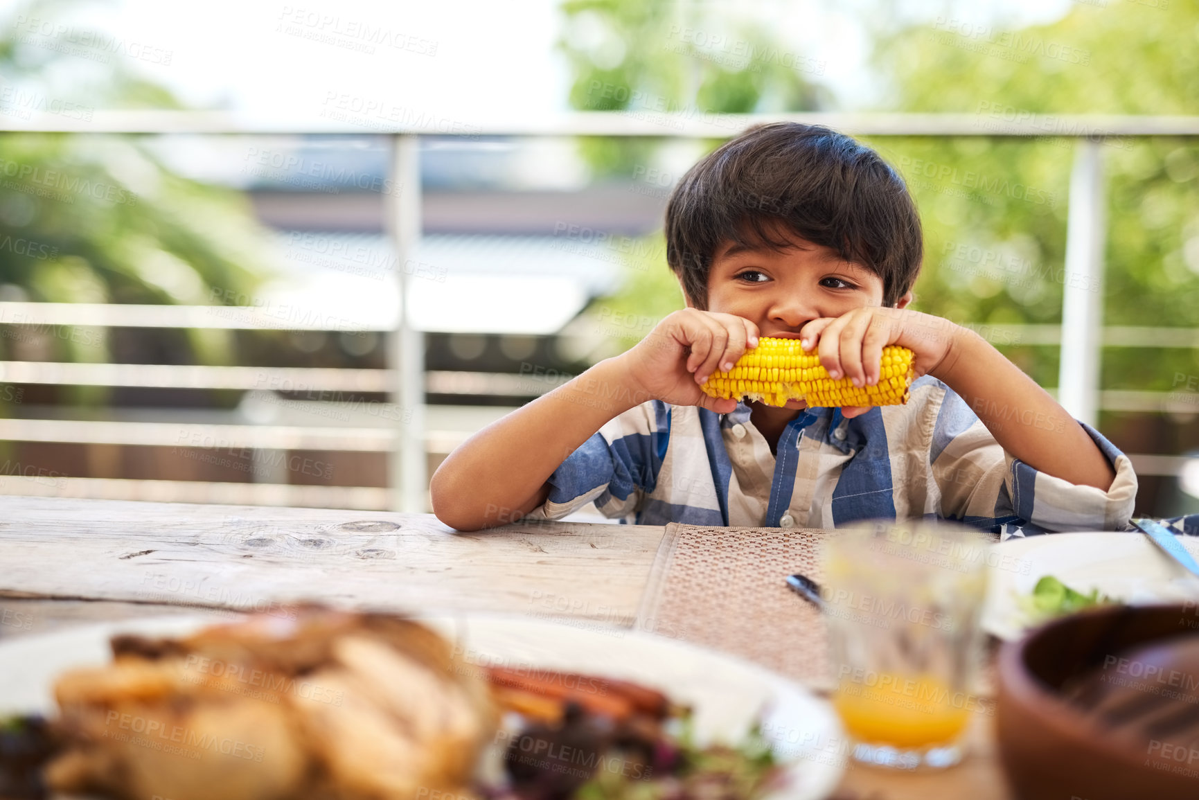 Buy stock photo Home, lunch and child with corn at backyard for healthy vegetables, nutrition and development. Outdoor, house and boy kid with food by table for afternoon meal, vitamins and eating of nutrients