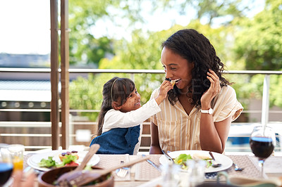 Buy stock photo Shot of an adorable little girl feeding her mother while enjoying a meal together around a table outdoors