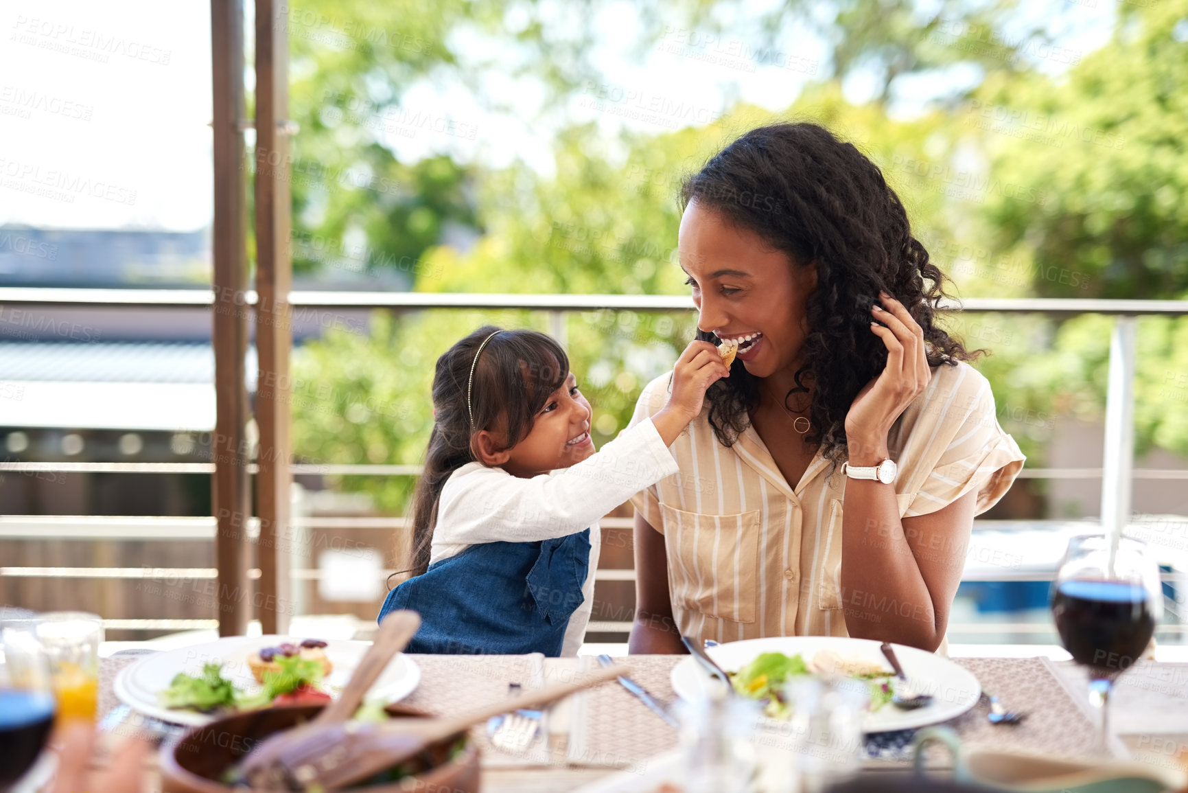 Buy stock photo Mom, girl and feeding by table for lunch with food for prepare feast, outdoor and together for festive holiday. Mother, daughter and home for thanksgiving celebration, tradition and bonding with love