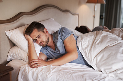 Buy stock photo Shot of a young man looking concerned while his girlfriend sleeps in the background in their bed at home