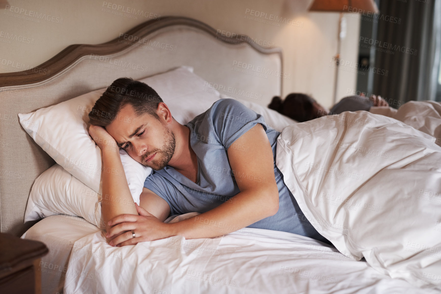 Buy stock photo Shot of a young man looking concerned while his girlfriend sleeps in the background in their bed at home