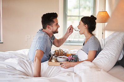 Buy stock photo Shot of an affectionate young couple enjoying breakfast in bed together in their bedroom at home