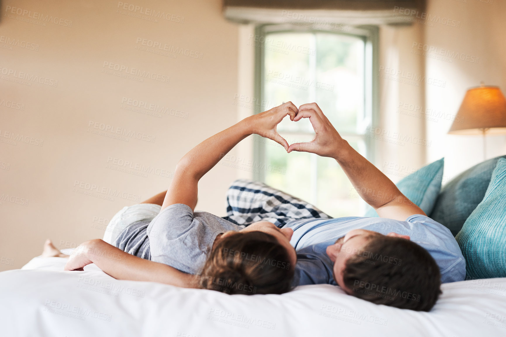 Buy stock photo Shot of an affectionate young couple making a heart shape with their hands in their bedroom at home
