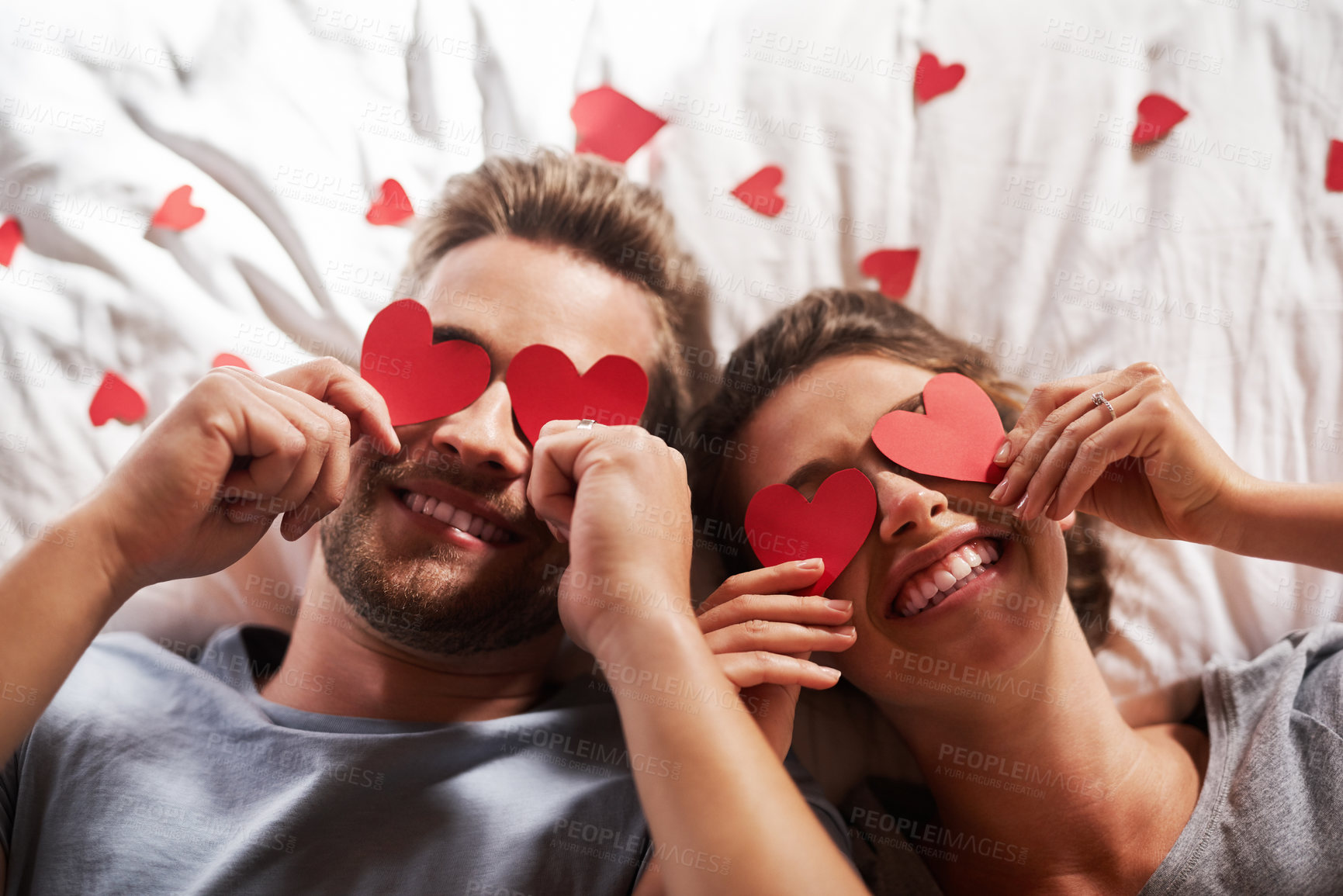 Buy stock photo Shot of an affectionate young couple covering their eyes with heart shapes in the bedroom at home