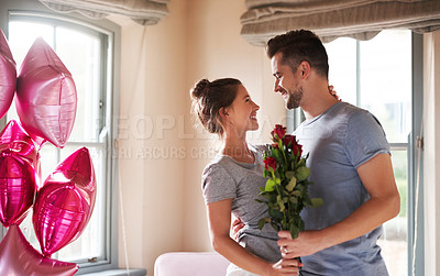 Buy stock photo Shot of a young man surprising his girlfriend with balloons and roses in their bedroom at home