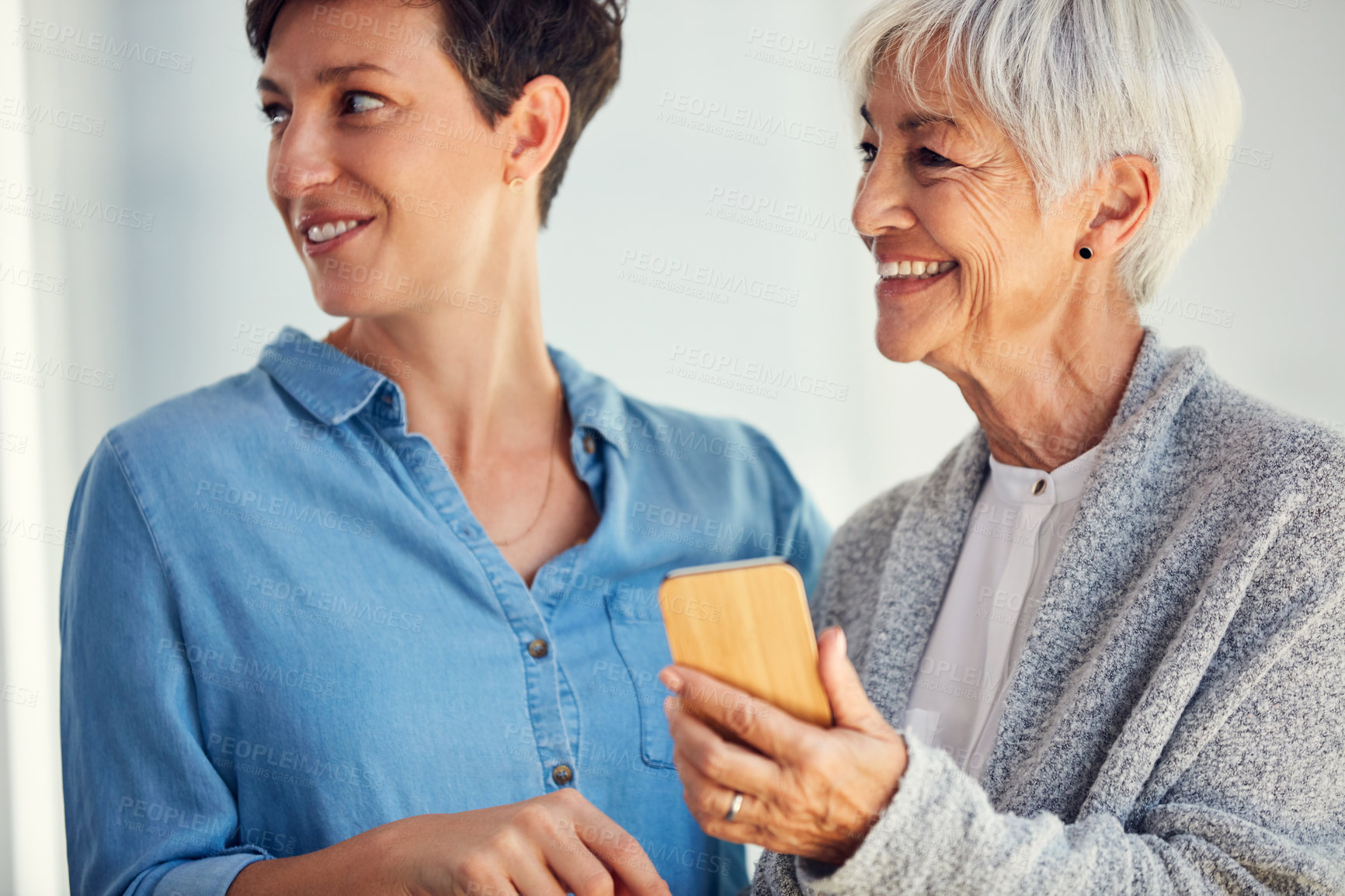 Buy stock photo Cropped shot of a happy senior woman and her daughter looking away while using a smartphone together