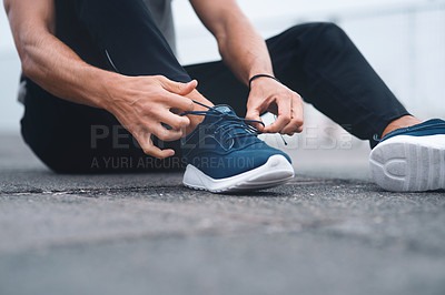 Buy stock photo Closeup shot of an unrecognisable man tying his laces while exercising outdoors