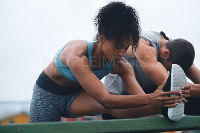Buy stock photo Shot of a sporty young woman stretching while exercising with her partner outdoors