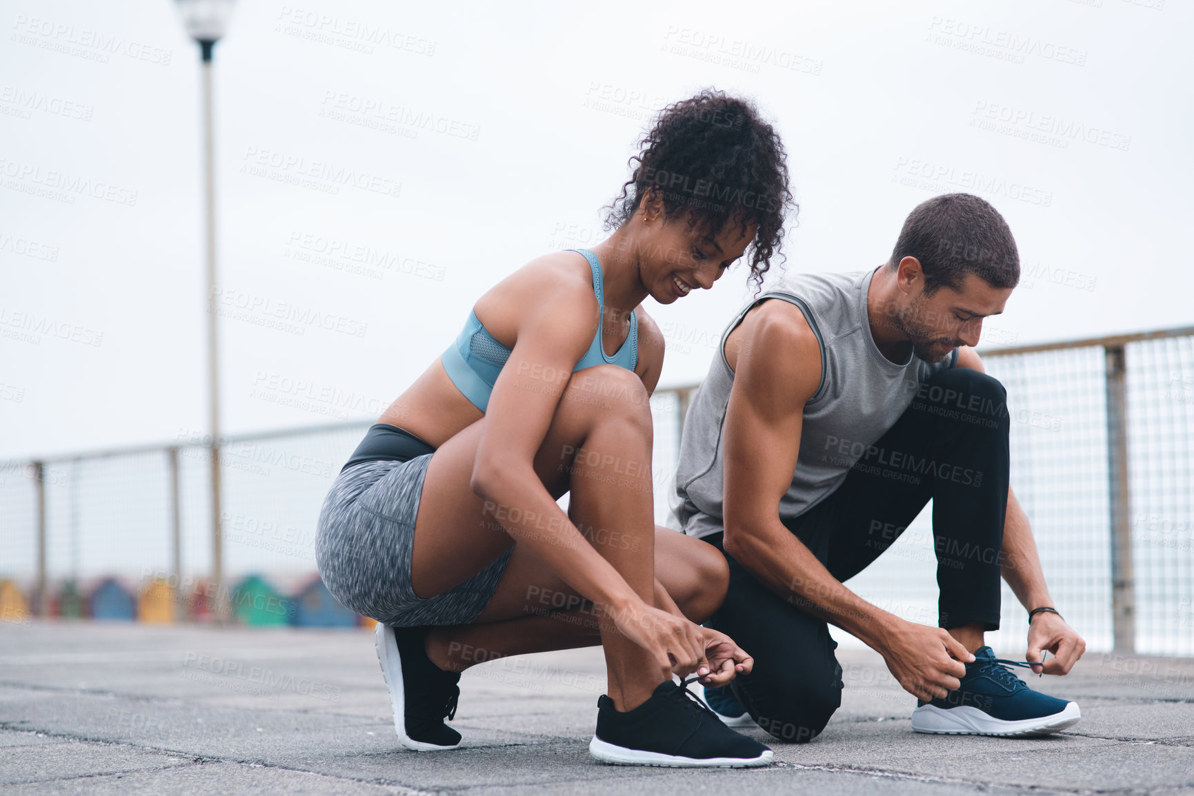 Buy stock photo Shot of two sporty young people tying their laces while exercising outdoors