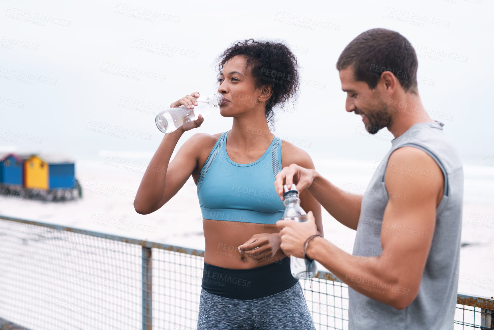 Buy stock photo Shot of two sporty young people drinking water while exercising outdoors