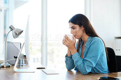 Buy stock photo Shot of a young businesswoman drinking coffee while working on a computer in an office