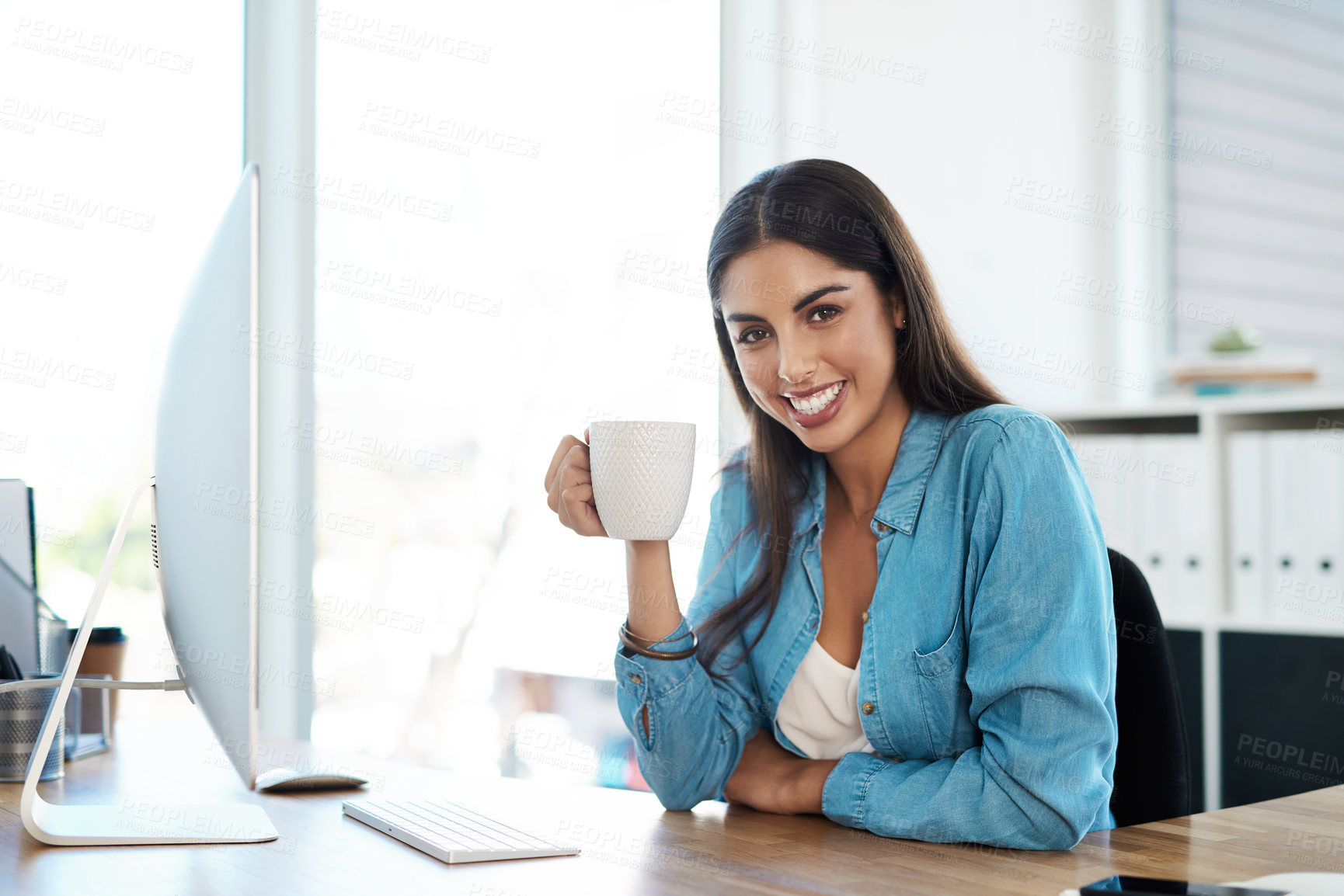 Buy stock photo Portrait of a young businesswoman drinking coffee while working on a computer in an office