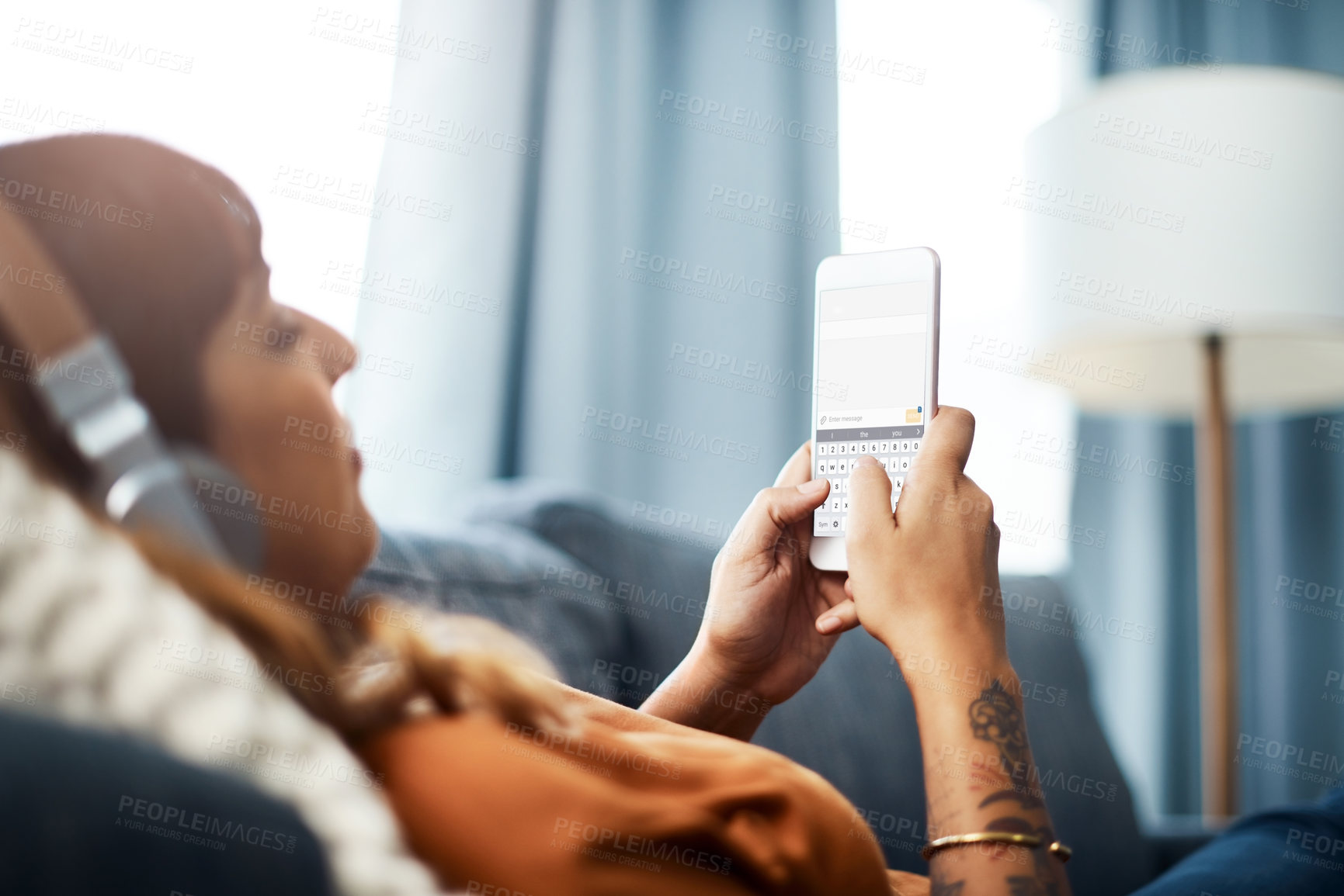 Buy stock photo Cropped shot of a young woman using her cellphone while relaxing on the sofa at home