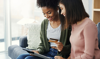 Buy stock photo Cropped shot of two attractive young women using a tablet together for online shopping while sitting on the sofa