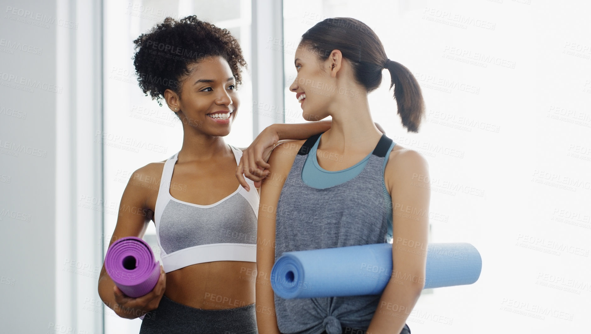 Buy stock photo Cropped shot of two attractive young women standing and holding yoga mats and posing before working out indoors