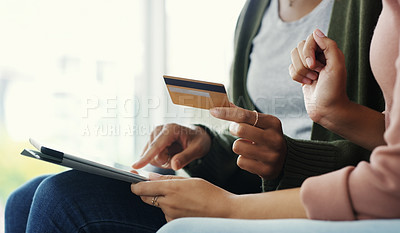Buy stock photo Cropped shot of two unrecognizable women using a tablet together for online shopping while sitting on the sofa