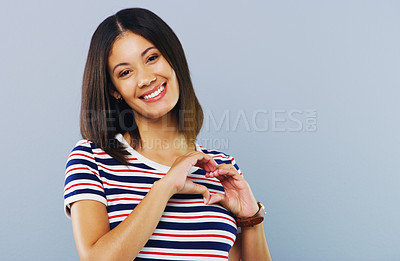 Buy stock photo Studio shot of a young woman making a heart shaped gesture against a grey background
