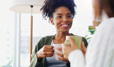 Buy stock photo Cropped shot of two attractive young women sitting together and drinking coffee while at home during the day