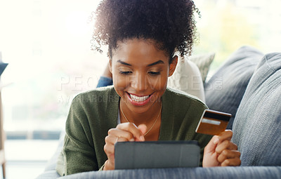 Buy stock photo Cropped shot of an attractive young woman using a tablet for online shopping while lying down on the sofa