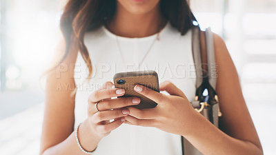 Buy stock photo Cropped shot of a businesswoman using a smartphone while walking through a modern office