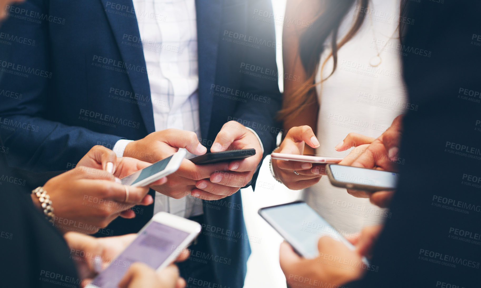Buy stock photo Cropped shot of a group of businesspeople standing in a circle and using their smartphones in a modern office