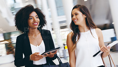 Buy stock photo Shot of two young businesswomen having a conversation while walking through a modern office