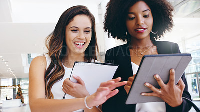 Buy stock photo Shot of two young businesswomen using a digital tablet while walking through a modern office