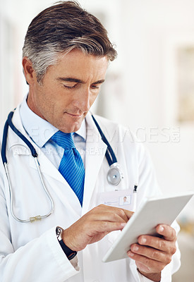 Buy stock photo Cropped shot of a handsome mature male doctor holding a digital tablet while standing in a hospital corridor