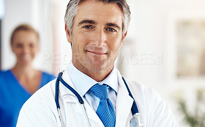 Buy stock photo Portrait of a handsome mature male doctor standing in the hospital with a female colleague in a the background