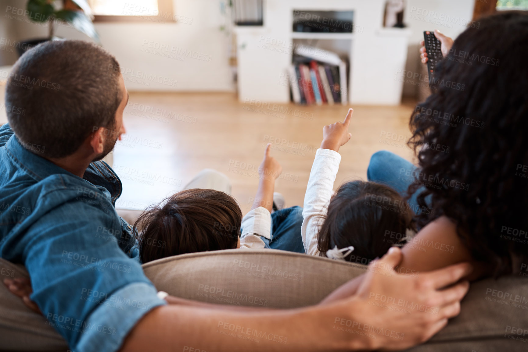 Buy stock photo Rearview shot of a couple watching something on the television with their two young kids