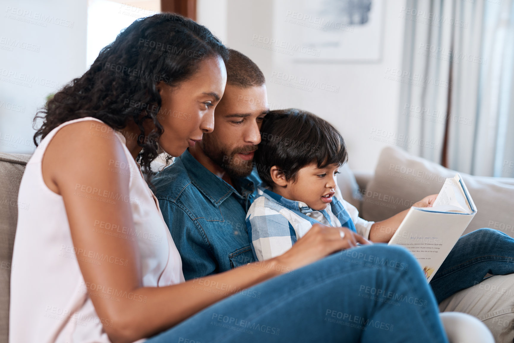 Buy stock photo Shot of a little boy reading a book while sitting with his parents