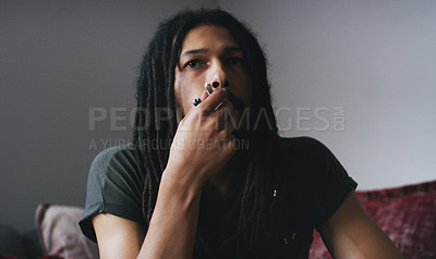 Buy stock photo Shot of a young man smoking a marijuana joint at home