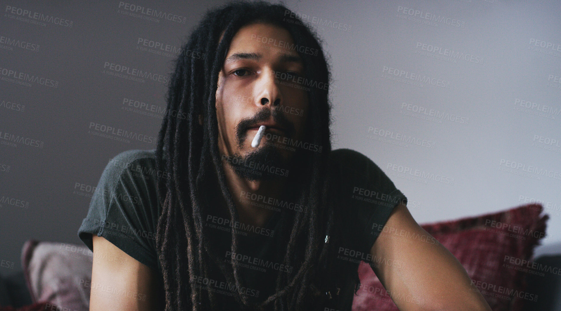 Buy stock photo Shot of a young man smoking a marijuana joint at home