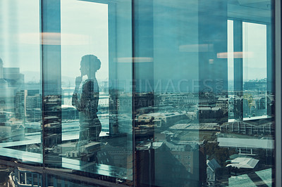 Buy stock photo Shot of a businesswoman standing inside a glass building with a reflection of the city in the background