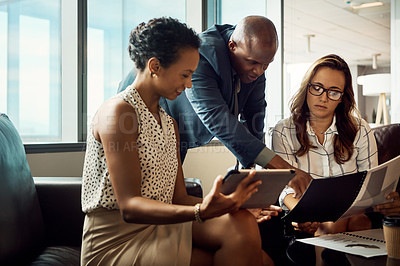 Buy stock photo Shot of a group of businesspeople using a digital tablet while going over some paperwork in their office