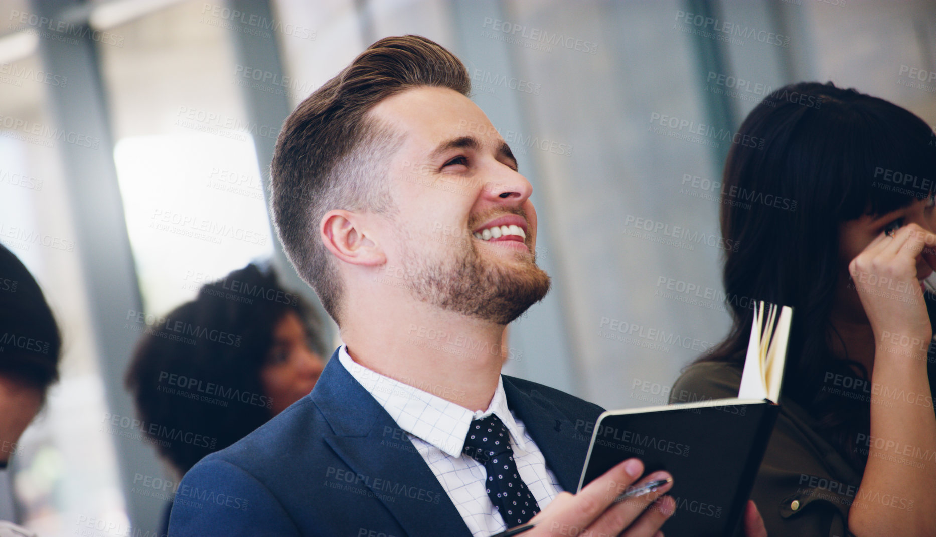 Buy stock photo Cropped shot of a handsome young businessman sitting with his colleagues and holding a notebook while in the office