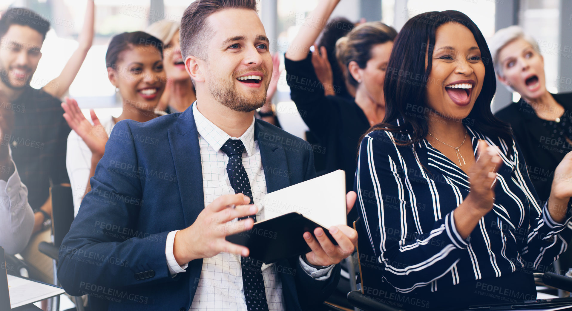 Buy stock photo Cropped shot of a handsome young businessman sitting with his colleagues and holding a notebook while in the office