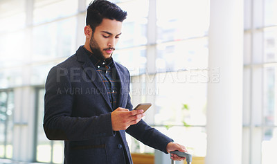 Buy stock photo Cropped shot of a handsome young businessman standing and using his cellphone while pulling a suitcase in the office